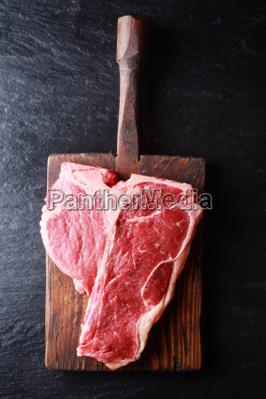 Foto Stock Bistecca alla fiorentina cruda sul tagliere di legno con mannaia da  cucina